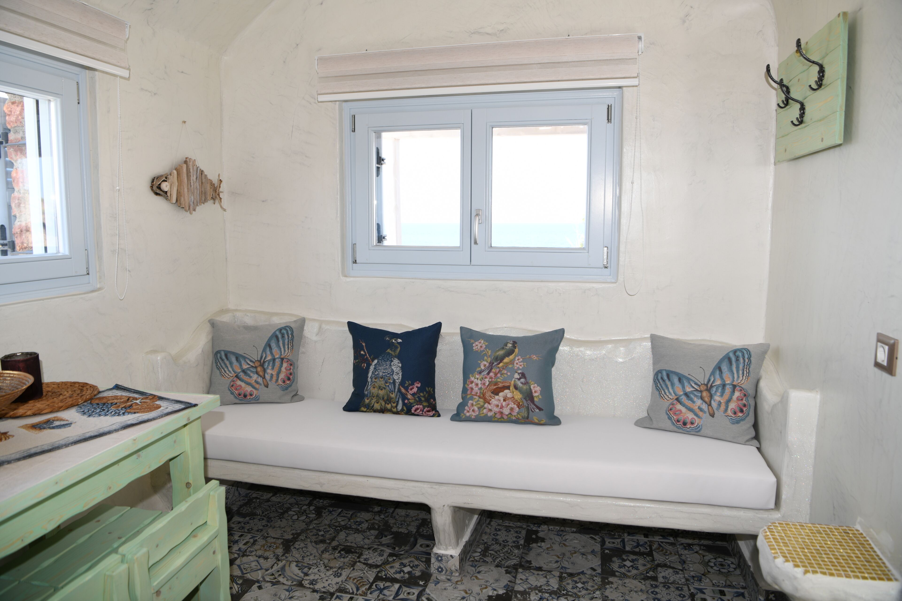 Ein weißes Sofa mit Kissen mit Schmetterlingsmotiv, ein grüner Tisch mit einer Dekoration und ein Fenster mit Blick.