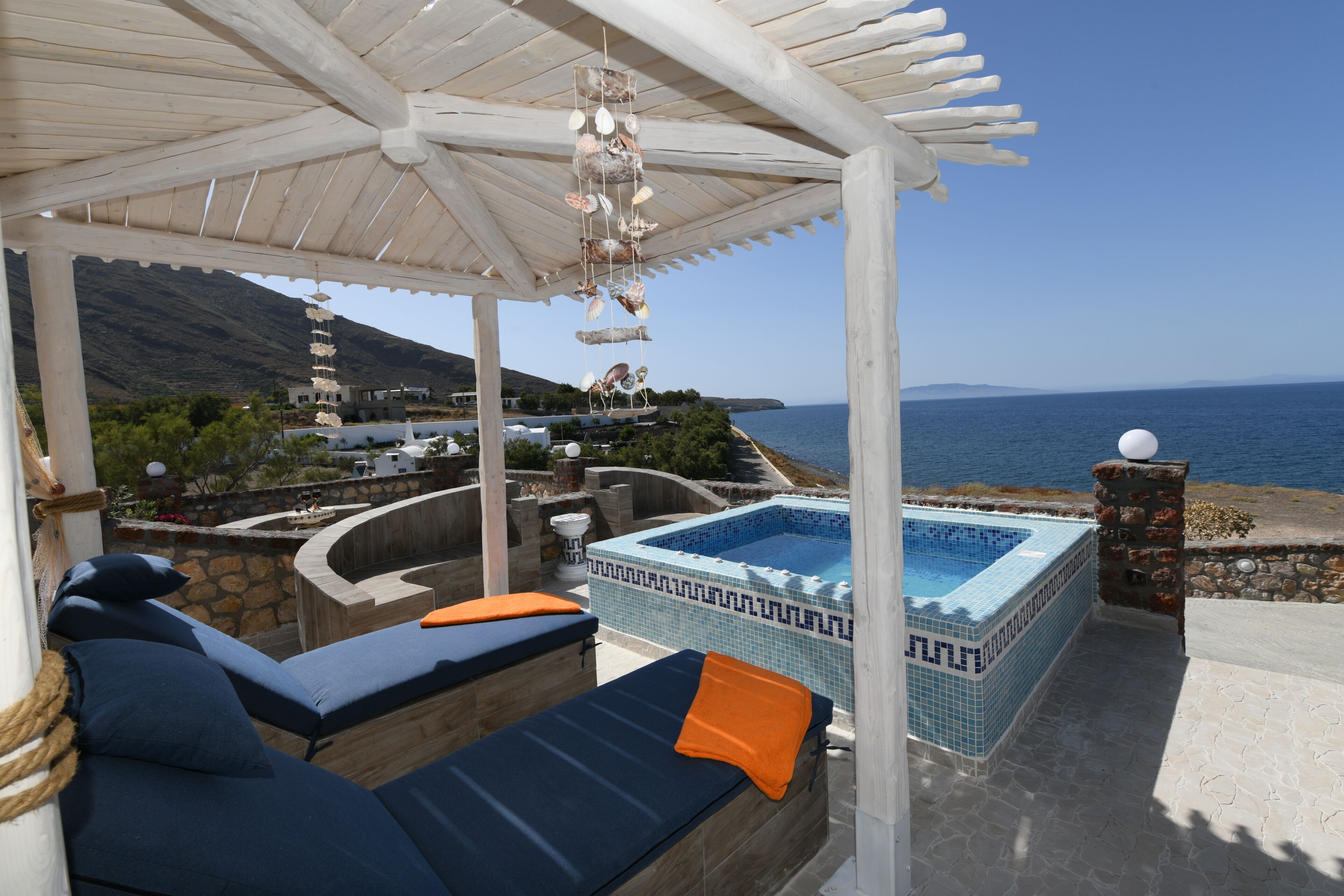 Un espacio exterior cubierto con un jacuzzi, sillones de descanso y vistas al mar.