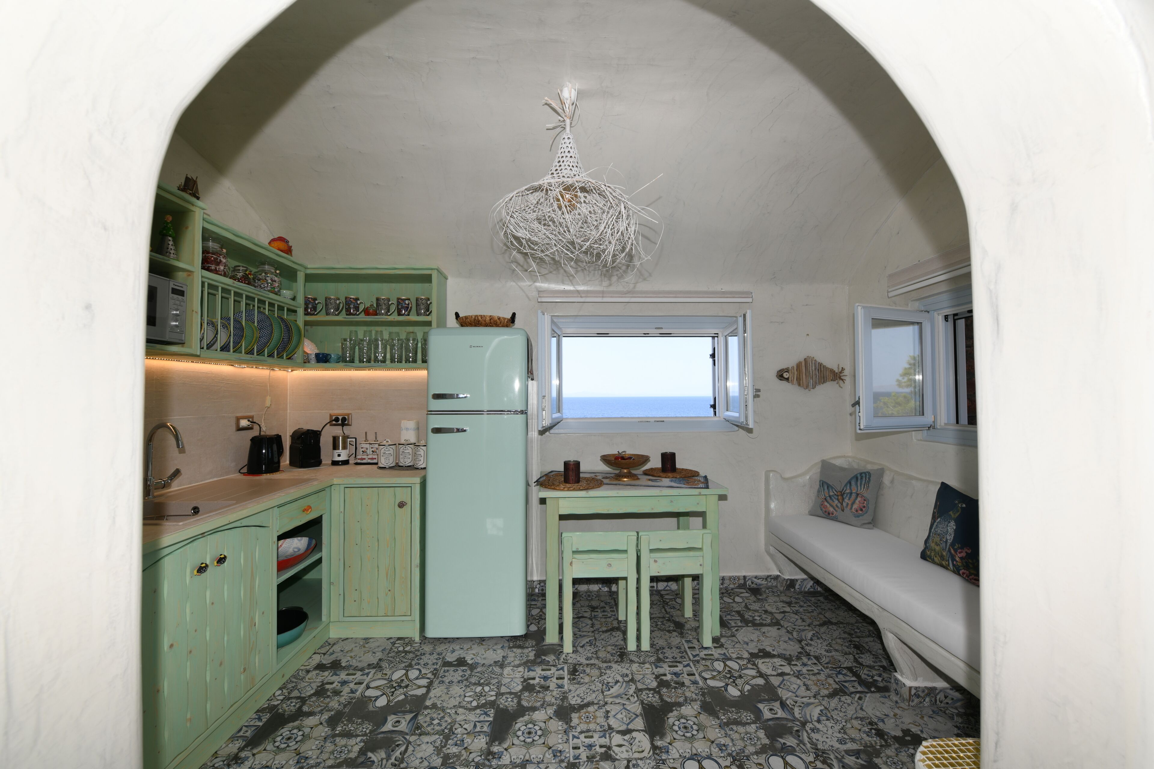 A compact kitchen with a refrigerator, sink, and a window overlooking the sea.