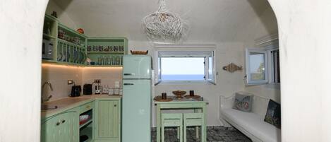 A compact kitchen with a refrigerator, sink, and a window overlooking the sea.