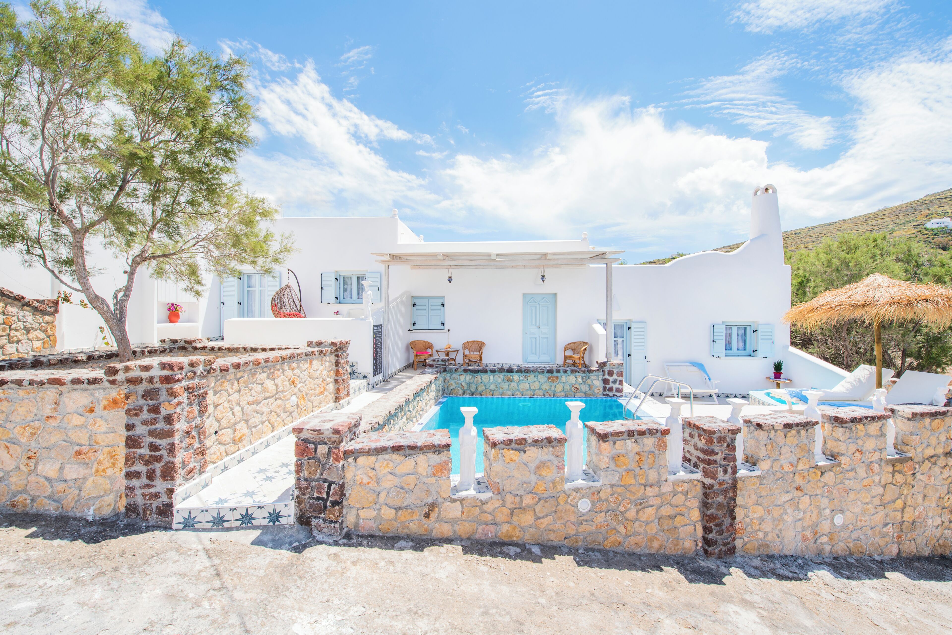 A white building with a swimming pool, stone walls, and outdoor seating.