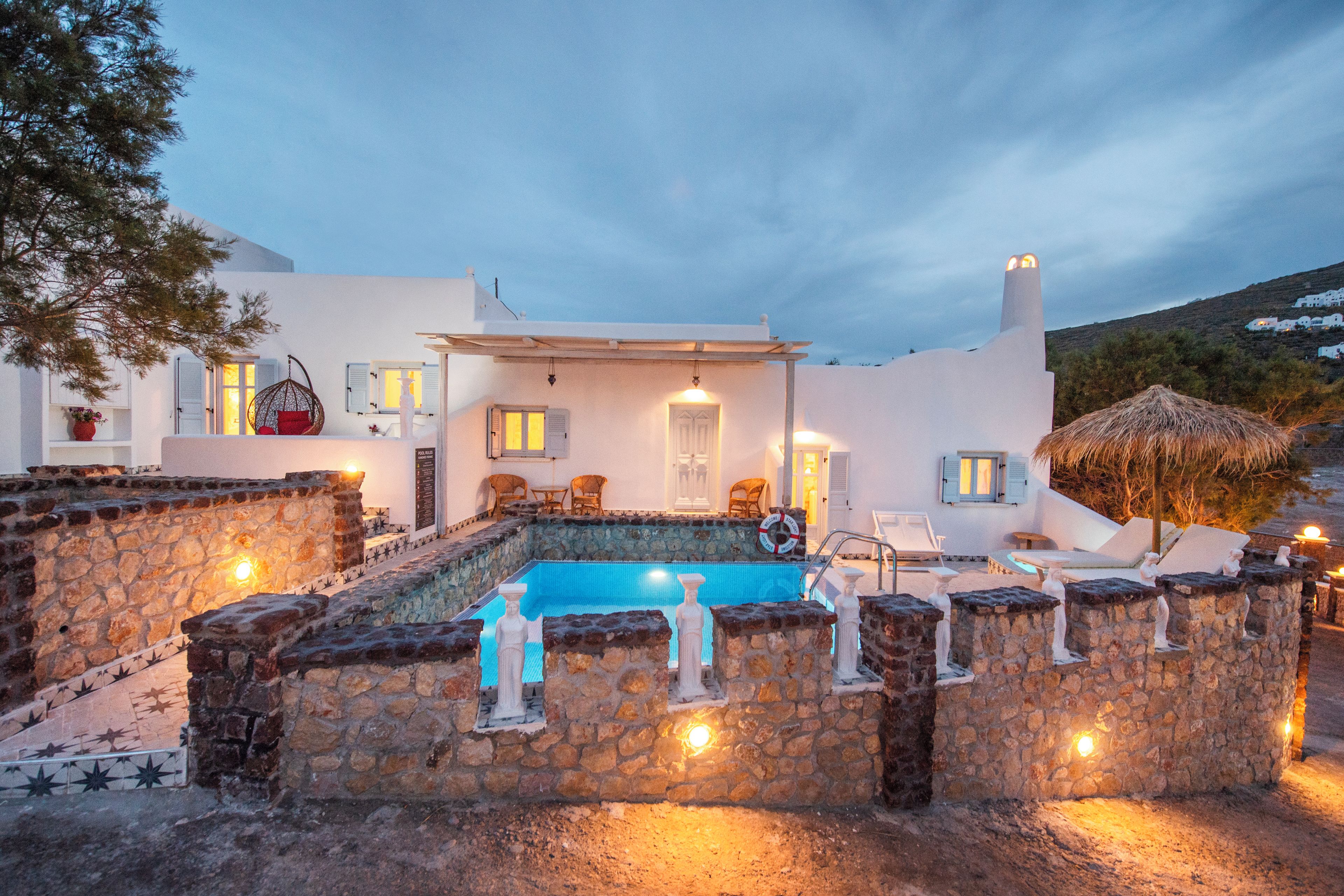 A white building with a swimming pool, stone walls, and outdoor seating.
