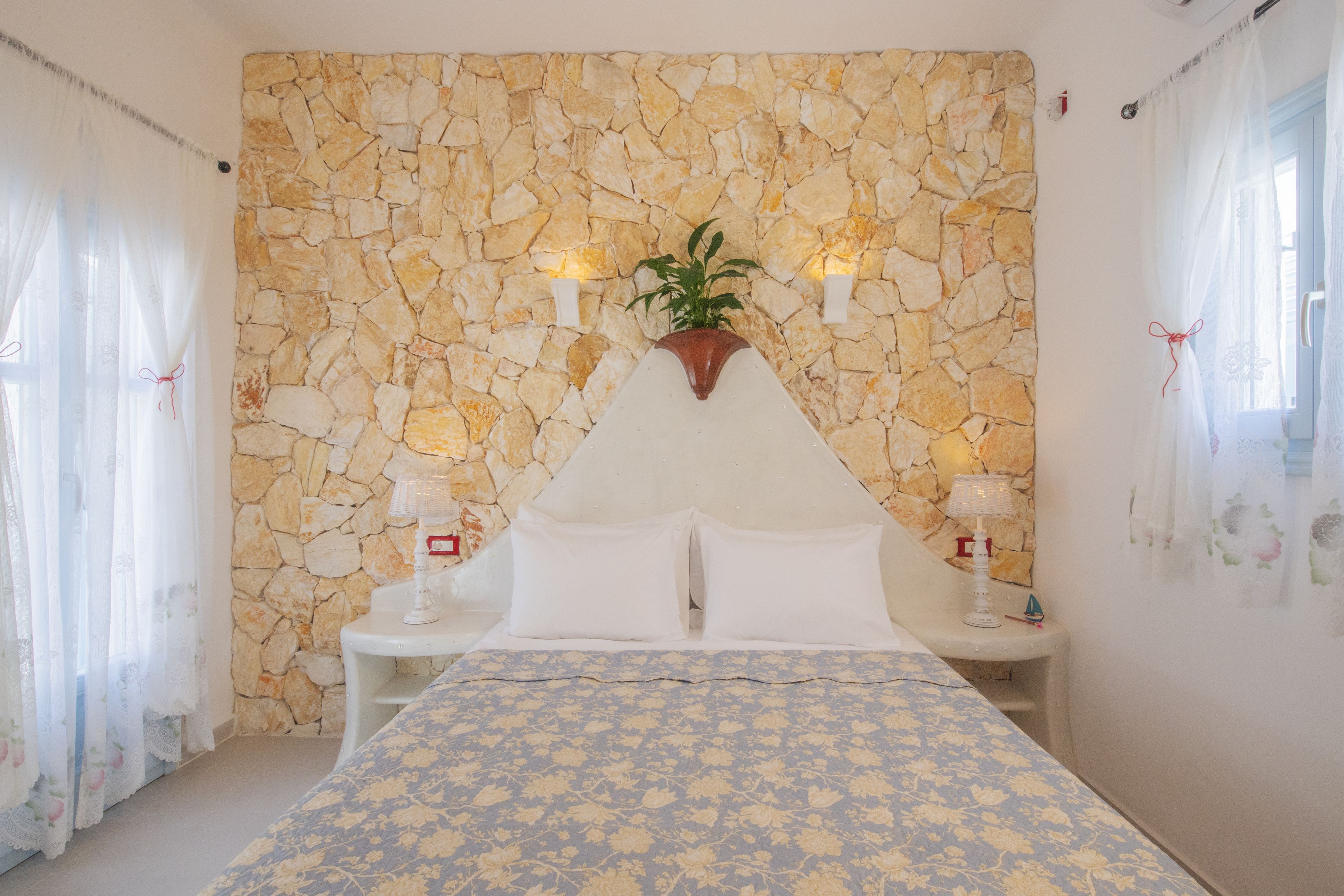 A bedroom with a stone wall, a bed with a floral bedspread, two bedside tables with lamps, and a plant on the wall.