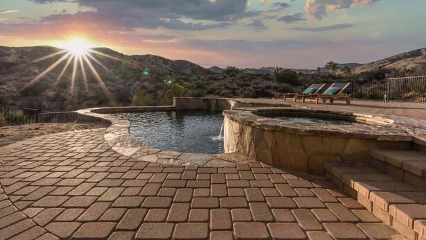 Ein Poolbereich mit Sonnenuntergangsblick, einer Pflasterterrasse und Liegestühlen.