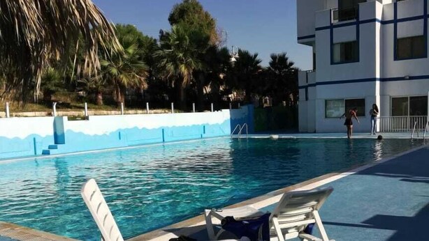 A swimming pool with lounge chairs and a building in the background.