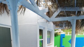 A blue and white play area with a thatched roof, a white wall, and a green fence.