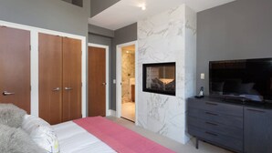 Un dormitorio con cama, televisor, armario y baño visible a través de una puerta abierta.