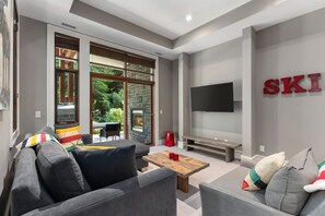 A modern living room with a grey sofa, a wooden coffee table, and a flat-screen TV mounted on the wall.