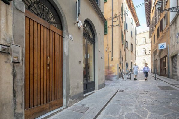A narrow street with buildings on either side, a wooden gate, and a pedestrian crossing sign.