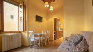 Una sala de estar acogedora con sofá, una mesa de comedor con sillas, una zona de cocina y un amplio ventanal con persianas.