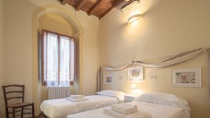 Una habitación con dos camas, una silla, un ventanal con cortinas y una obra de arte en la pared.