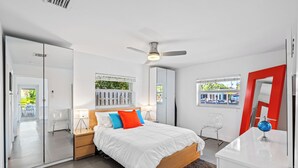 A modern bedroom with a large bed, a ceiling fan, and a view of the outdoors through a window.