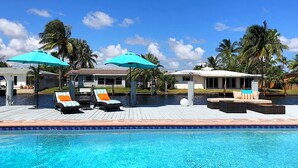 A swimming pool with lounge chairs and umbrellas, surrounded by palm trees and a clear blue sky.
