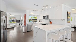 A modern kitchen with white cabinetry, a large island with bar stools, stainless steel appliances, and a view of the outdoors.