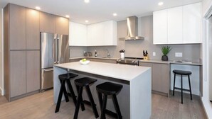 A modern kitchen with stainless steel appliances, a central island with stools, and white cabinetry.