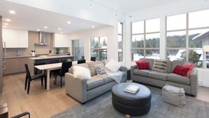 A modern living space with a kitchen, dining area, and seating area with large windows.
