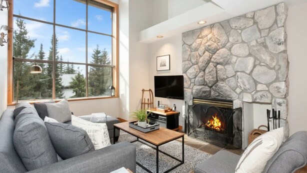 A modern living room with a stone fireplace, a large window, and a grey sofa. - Whistler retreat w/ private hot tub & ski access (Whistler)
