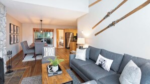 A modern living room with a grey sofa, a wooden coffee table, and a dining area with a table and chairs. - Whistler retreat w/ private hot tub & ski access (Whistler)
