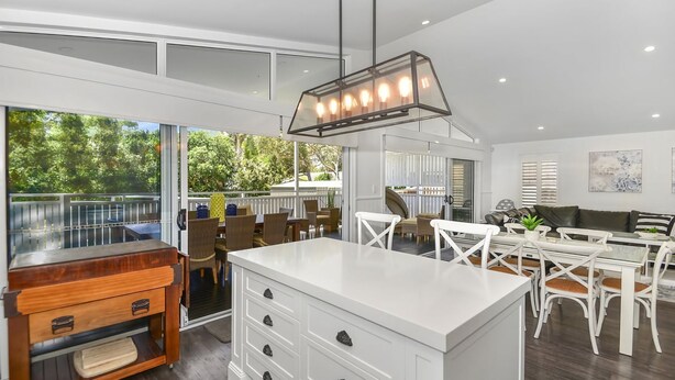 Una cocina moderna con armarios blancos, una isla central y una zona de comedor con mobiliario blanco.