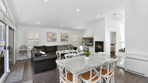 Un espacio de estar moderno con comedor, sofá, televisor, chimenea y vistas al exterior.