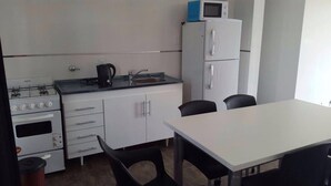 A compact kitchen with a gas stove, microwave, sink, and a small refrigerator. There is a table with two chairs and a window providing natural light. - Mi Gran Amor Termas (San José)