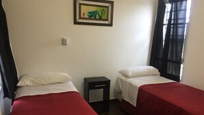 A room with two beds, each with a red bedspread and white pillows, a small black nightstand, and a framed picture on the wall. - Mi Gran Amor Termas (San José)