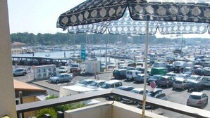 A balcony with a white metal table and a yellow chair, overlooking a parking lot and a marina. - CAP SUD residence- Flat for 3 persons close to marina (CAPBRETON)