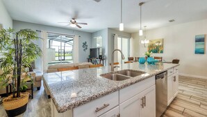 A modern kitchen with a granite countertop, stainless steel sink, and white cabinetry. There is a ceiling fan, pendant lights, and a large window providing natural light. - SL3059 - 4BR house with private pool in Kissimmee (Kissimmee)