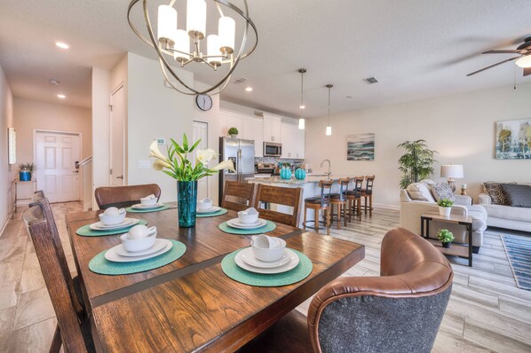 A dining area with a wooden table set for four, surrounded by chairs. There is a kitchen in the background with white cabinets and a microwave. - 3059 - Beautiful Townhome Private Pool Near Disney (Kissimmee)