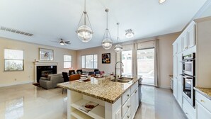 Een ruime keuken met een centraal kookeiland, witte kasten en een groot raam voor natuurlijk licht.