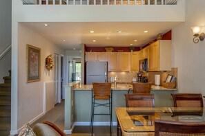 A modern kitchen with wooden cabinets, a central island with bar stools, and a dining area with a glass table and chairs.