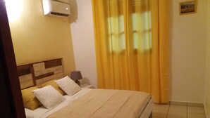 A bedroom with a bed, a nightstand, a lamp, curtains, and an air conditioning unit. - Villa Ponm Kann 'L, breathtaking sea / mountain view (DESHAIES)