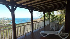 A covered outdoor area with wooden flooring, white railings, and two white lounge chairs. - Villa Ponm Kann 'L, breathtaking sea / mountain view (DESHAIES)
