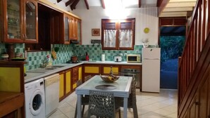 A kitchen with wooden cabinets, a washing machine, a dining table with chairs, and a microwave. - Villa Ponm Kann 'L, breathtaking sea / mountain view (DESHAIES)