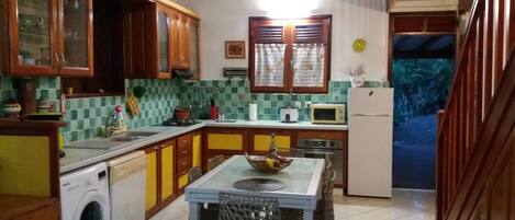 A kitchen with wooden cabinets, a washing machine, a dining table with chairs, and a microwave.
