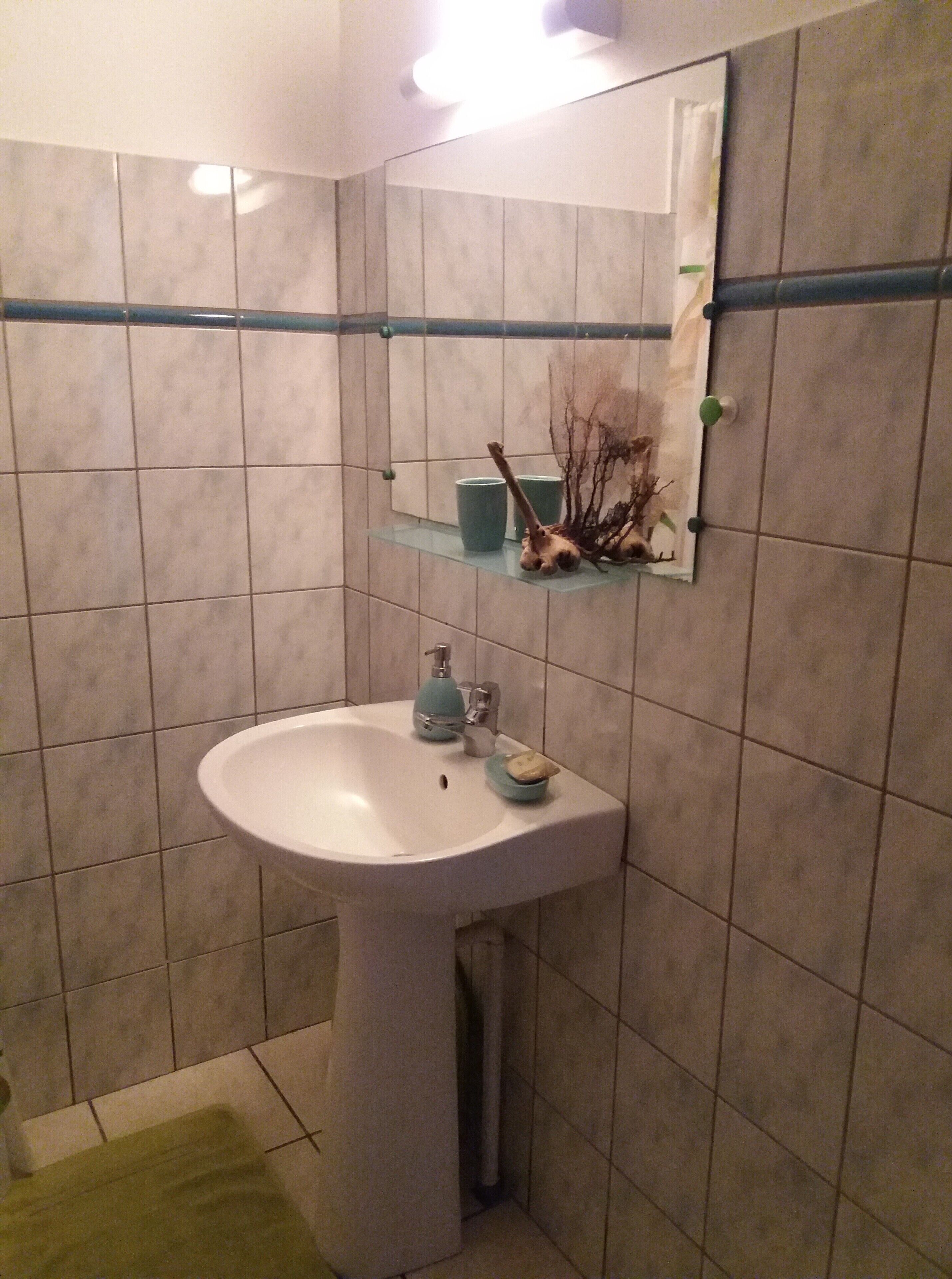 Une salle de bain avec un lavabo blanc, un miroir et une étagère contenant des articles de toilette.