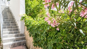Una scala conduce a un edificio bianco con un giardino adornato da fiori rosa e vegetazione verde.