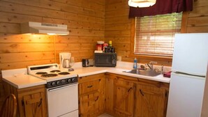 A compact kitchen with wooden cabinets, a stove, a microwave, and a refrigerator. - Tranquil Cabin- Perched on Mountain Top boasting jacuzzi for two and expansive deck with views! Trail & Cave on Property! (Eureka Springs)