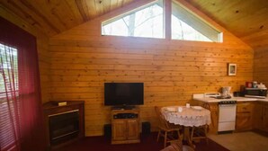 A cozy cabin interior with a wooden interior, a television, a dining table, and a kitchen area. - Tranquil Cabin- Perched on Mountain Top boasting jacuzzi for two and expansive deck with views! Trail & Cave on Property! (Eureka Springs)