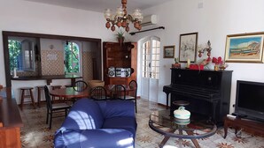 Un salon avec un canapé bleu, un piano, une télévision et un coin repas comprenant des chaises et une table.