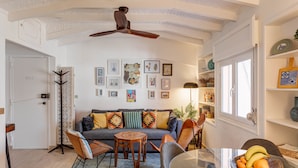 Un salon comprenant un canapé, des fauteuils, une table basse, un ventilateur de plafond et des œuvres d’art murales.