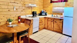 A compact kitchen with wooden walls, a dining table, and basic appliances. - Tranquil Cabin- Perched on Mountain Top boasting jacuzzi for two and expansive deck with views! Trail & Cave on Property! (Eureka Springs)