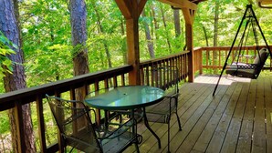 A wooden deck with a table and chairs, surrounded by trees. - Tranquil Cabin- Perched on Mountain Top boasting jacuzzi for two and expansive deck with views! Trail & Cave on Property! (Eureka Springs)