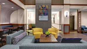 Een hotel lobby met een modern design, met een zithoek met banken en stoelen, een salontafel met appels, en een groot abstract schilderij aan de muur.