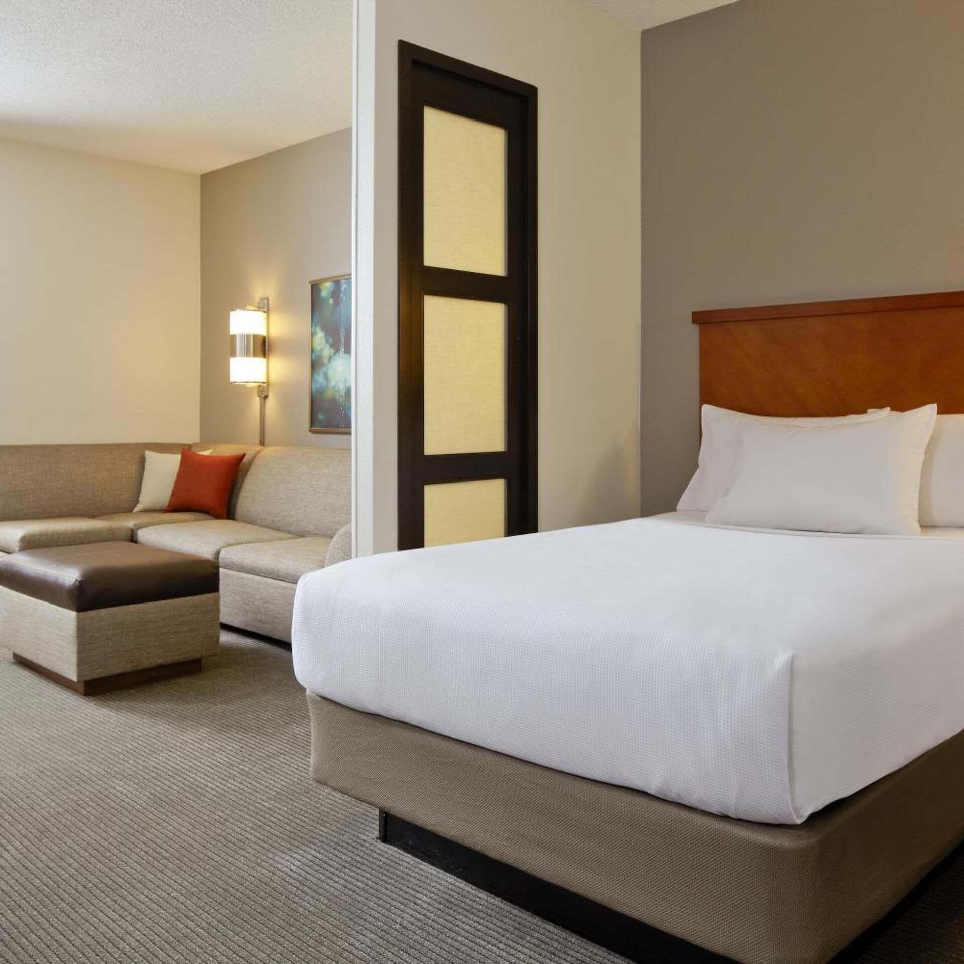 Een hotelkamer met een groot bed, een bank, een klein poufje, een wandlamp en een schilderij.
