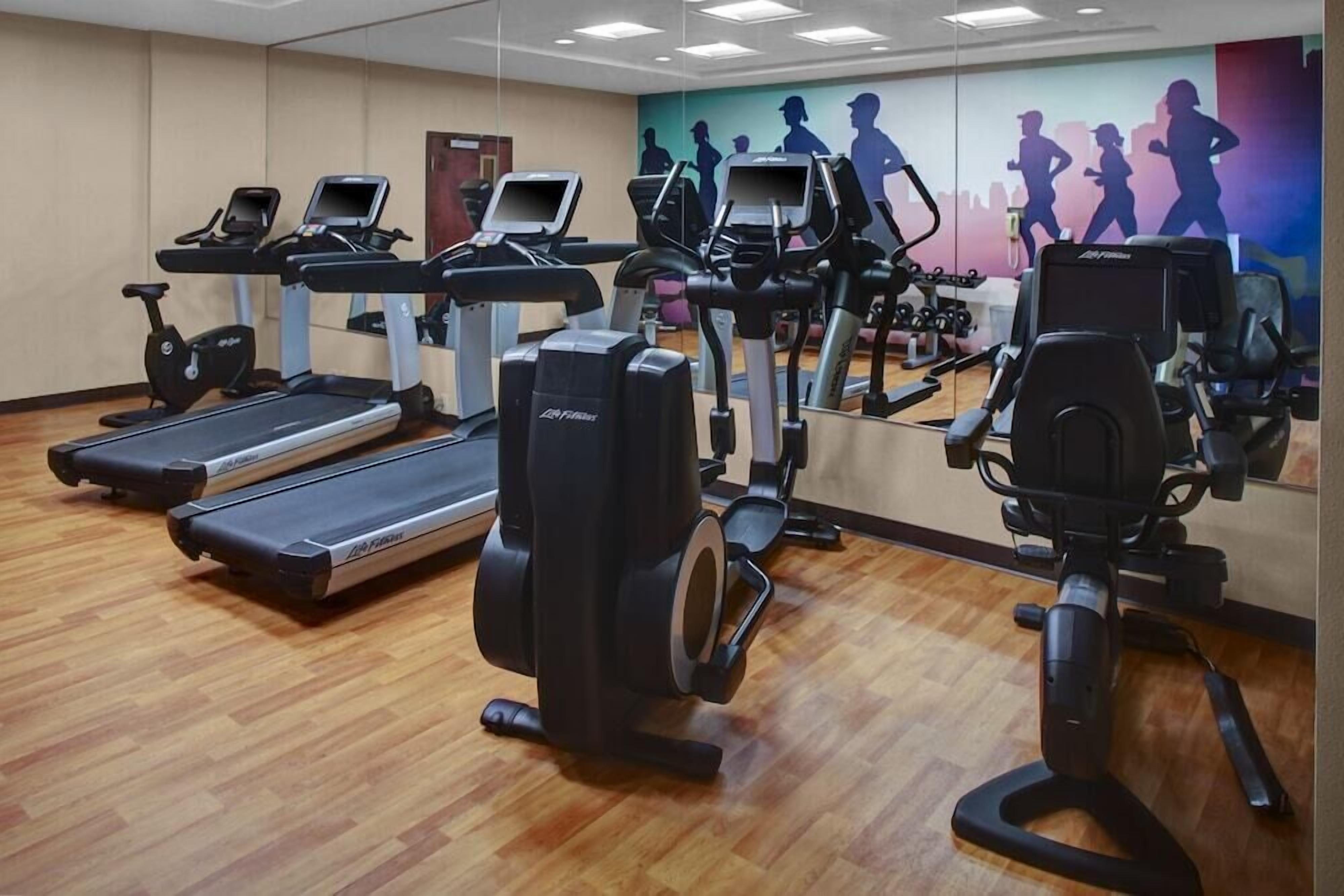 Une salle de sport équipée de tapis de course, de vélos elliptiques et d’un mur recouvert de miroirs.
