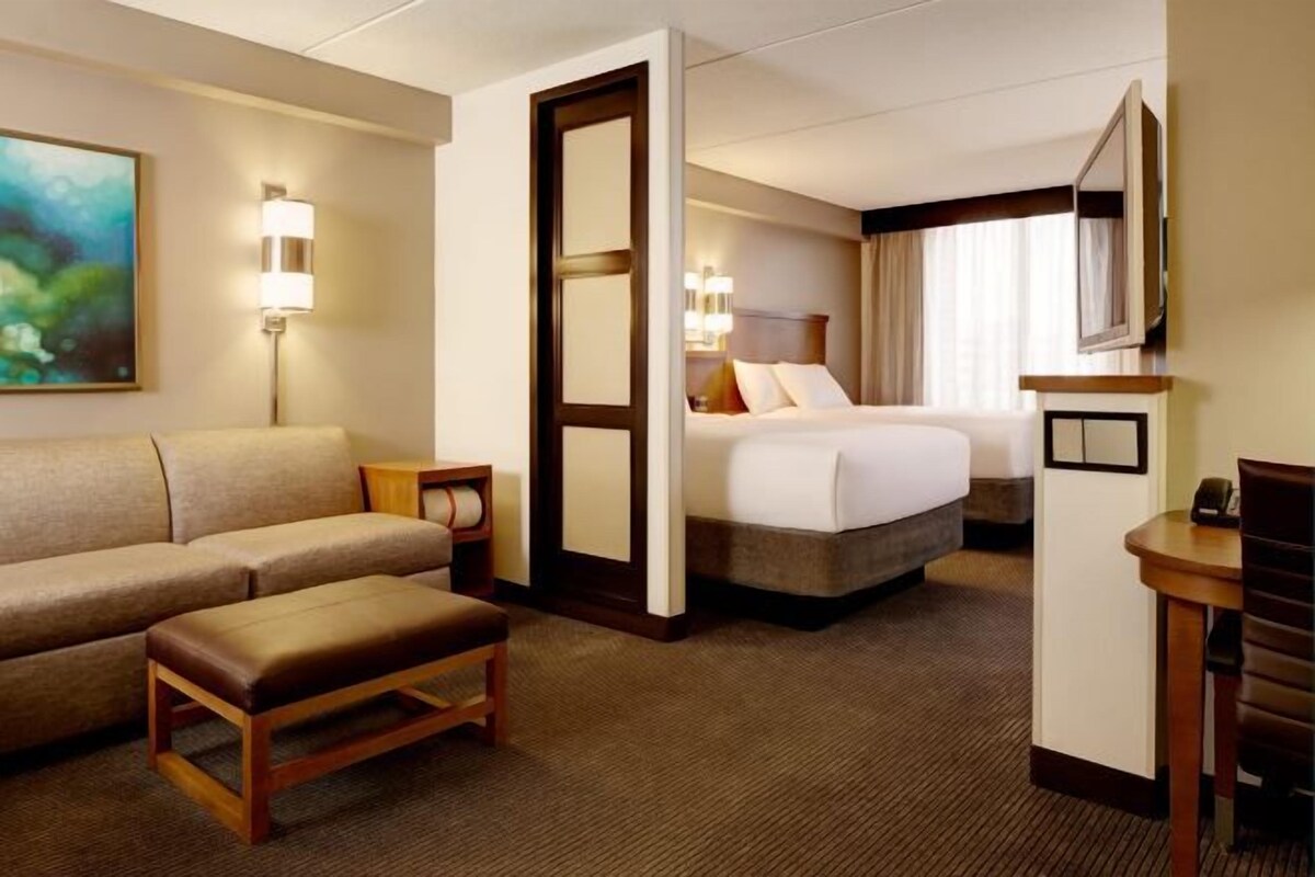 Een hotelkamer met een bed, een bank, een klein tafeltje, een televisie en een schilderij aan de muur.
