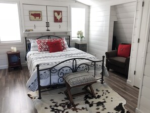 A bedroom with a bed, a small bedside table, a chair, and a cowhide rug. - Private Loft above the barn on horse ranch (Pilot Hill)