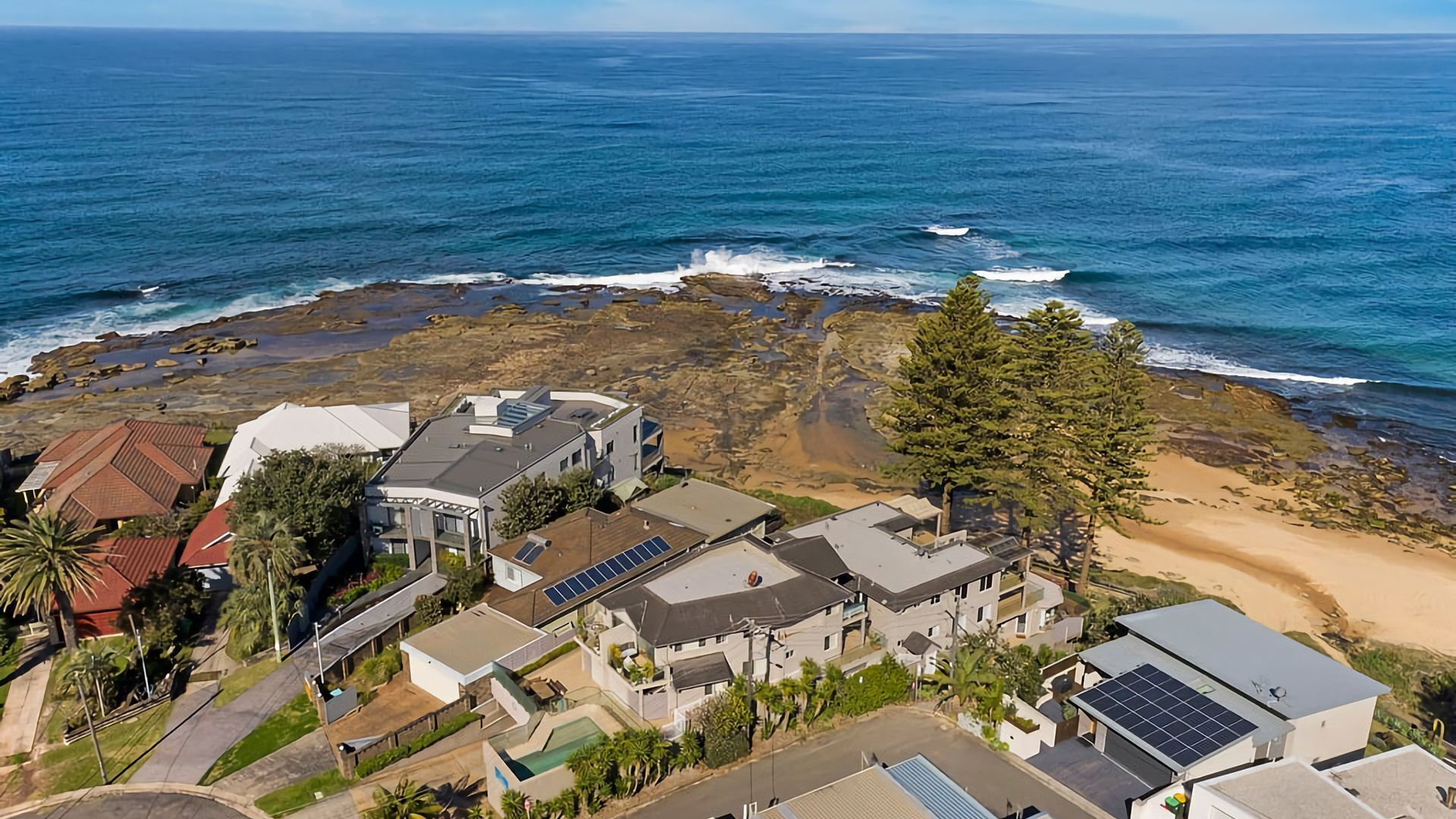A coastal residential area with houses, solar panels, and a rocky shoreline.