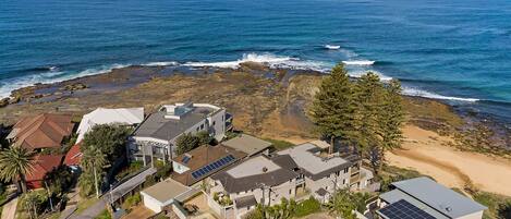 A coastal residential area with houses, solar panels, and a rocky shoreline.